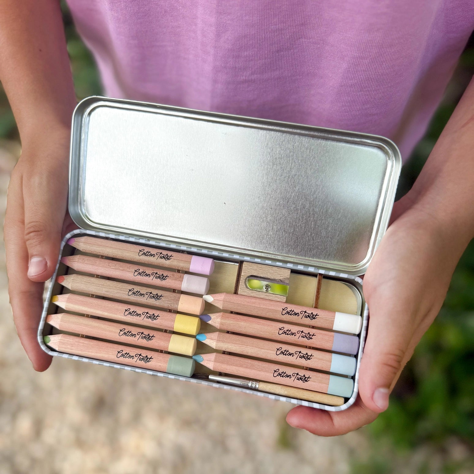 Metallic pencil case with colored pencils held by a person wearing a purple shirt.
