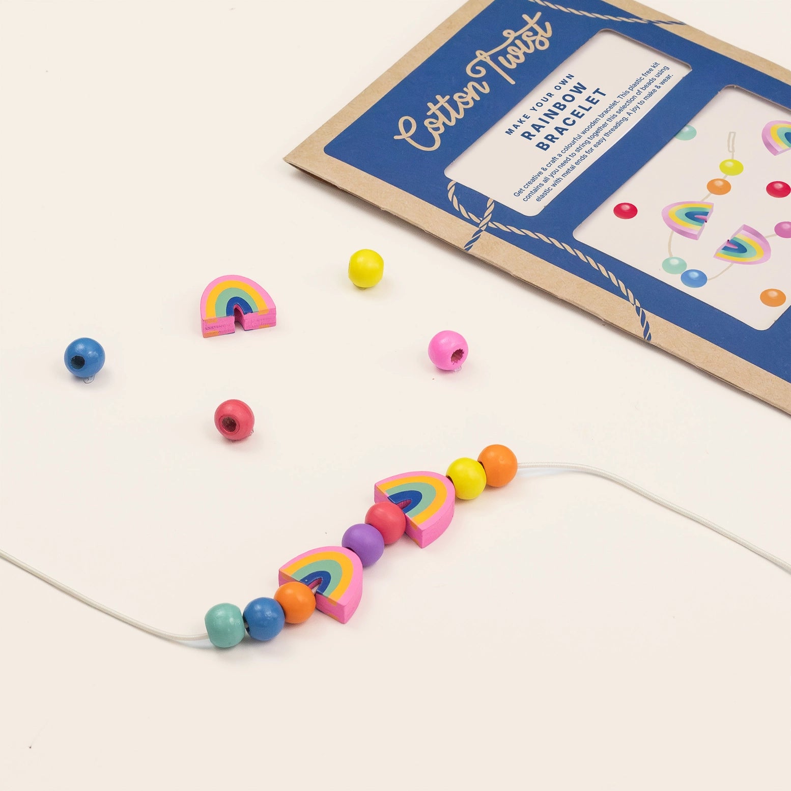 Colorful bead bracelet with rainbow shapes next to a craft kit on a beige background