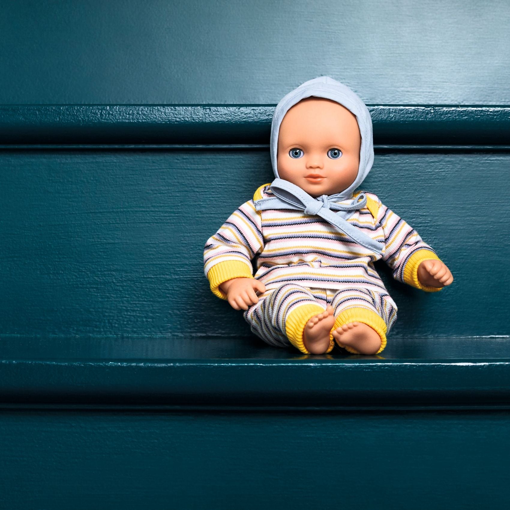 Baby doll in striped outfit and bonnet sitting on a blue surface
