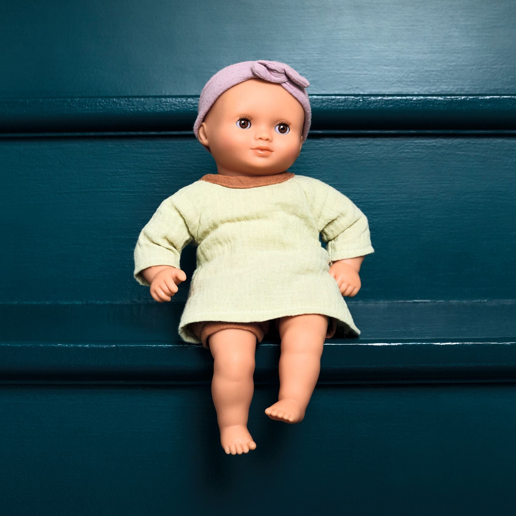 Doll wearing a light green dress and purple headband on a dark blue background