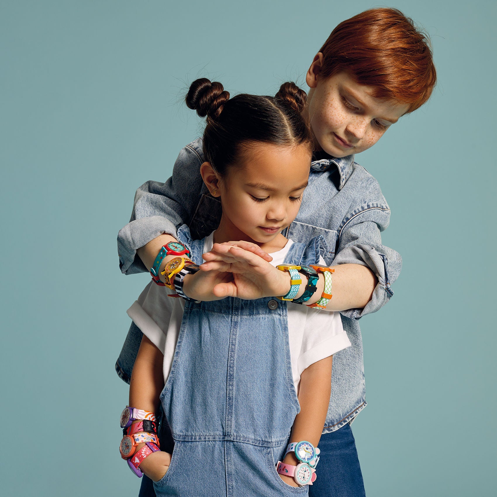Two children wearing colorful Djeco watches on a plain background