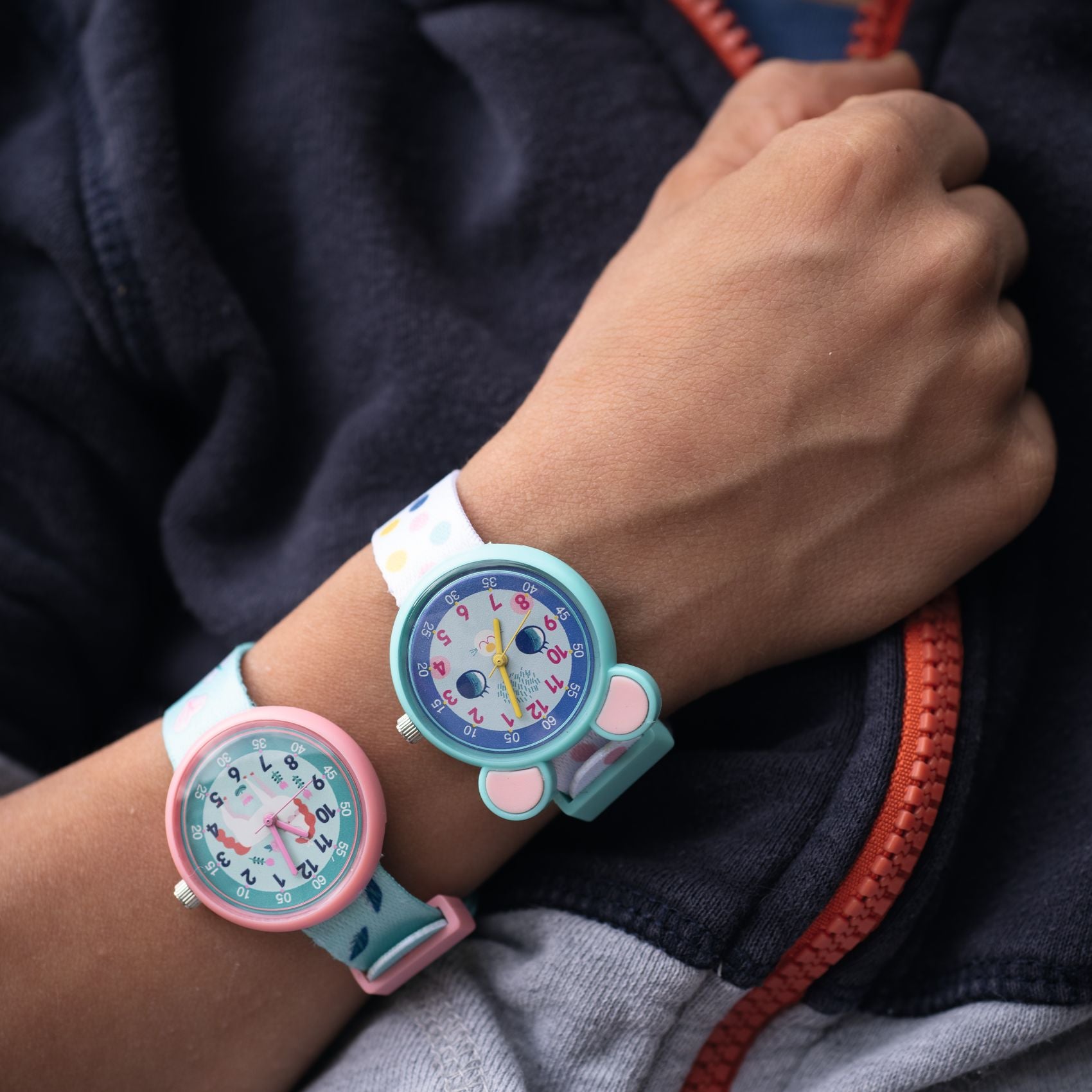Two colorful children's watches on a person's wrist with a dark jacket background.