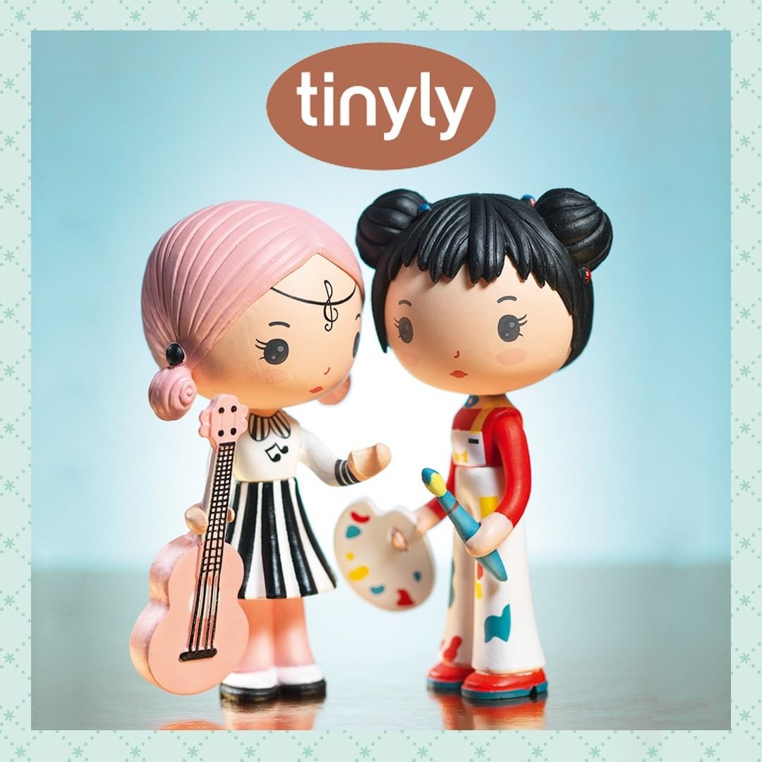 Two figurines, one with pink hair holding a guitar and the other with black hair holding a paintbrush, on a light blue background with 'tinyly' branding.