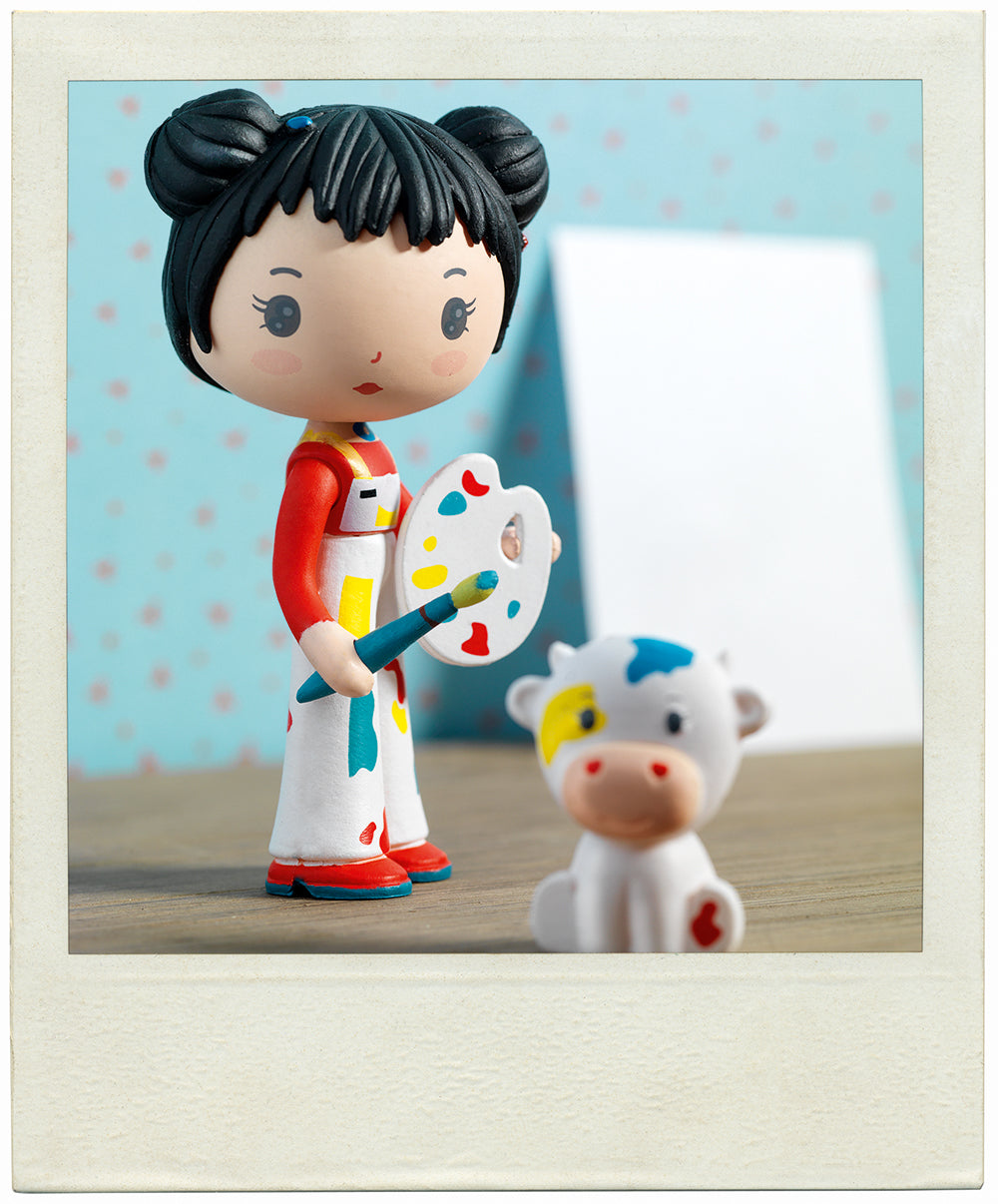 Colorful figurine of a painter with a cow toy on a wooden surface.