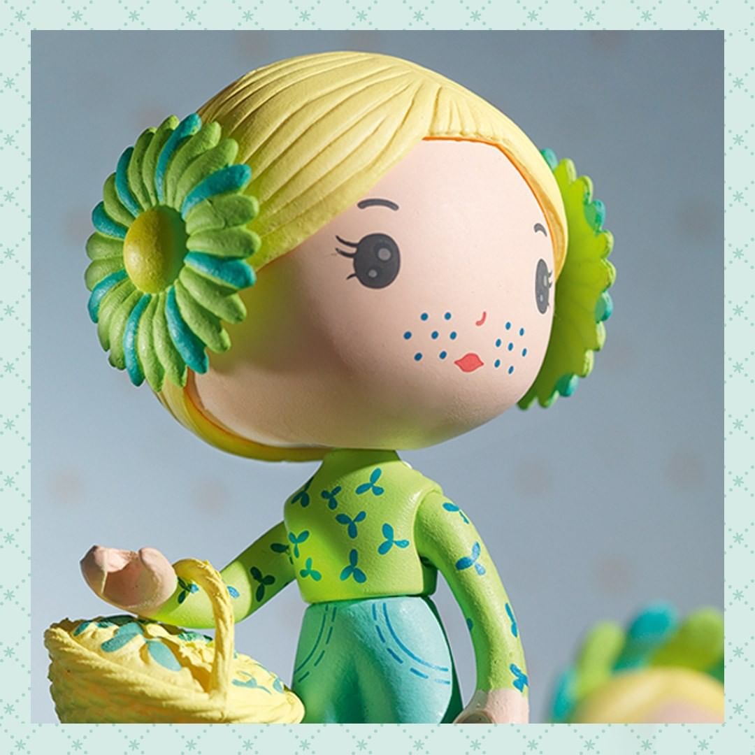 Toy figure with blonde hair and green flower accessory on a light blue background