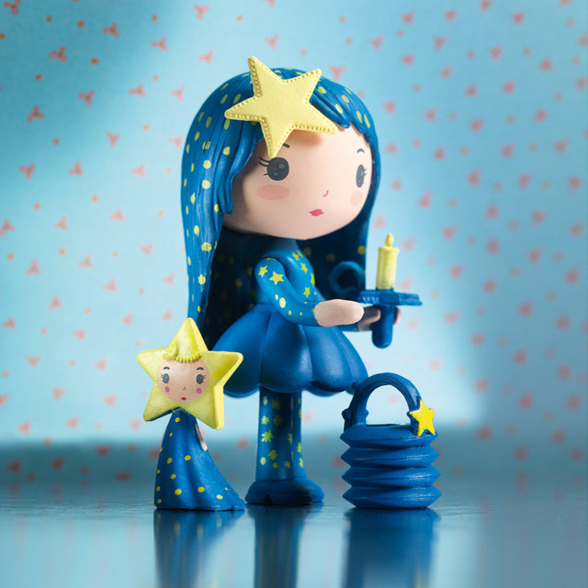 Toy figure with blue hair and outfit, holding a candle against a blue background with pink hearts.