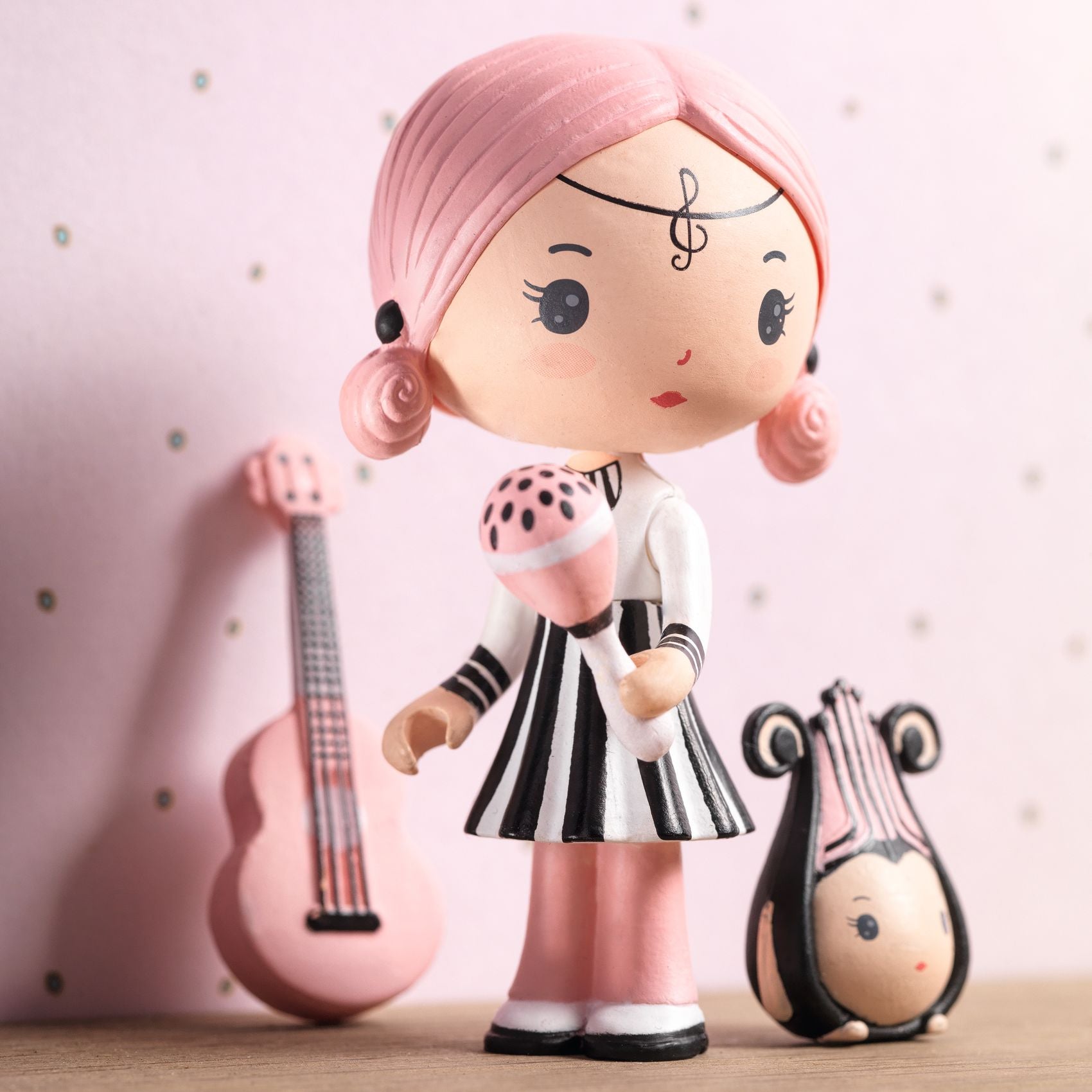 Toy figure with pink hair and a black and white outfit, standing next to a pink guitar and a small figure.