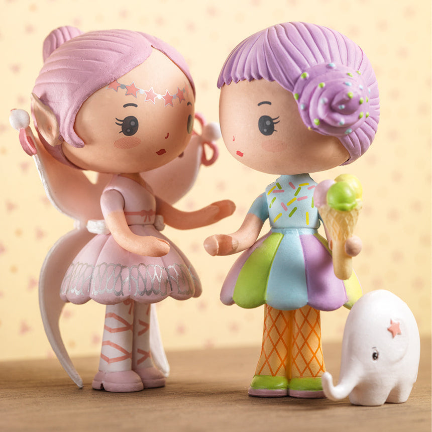 Two colorful figurines with pastel hair and dresses, standing next to a small white elephant toy.