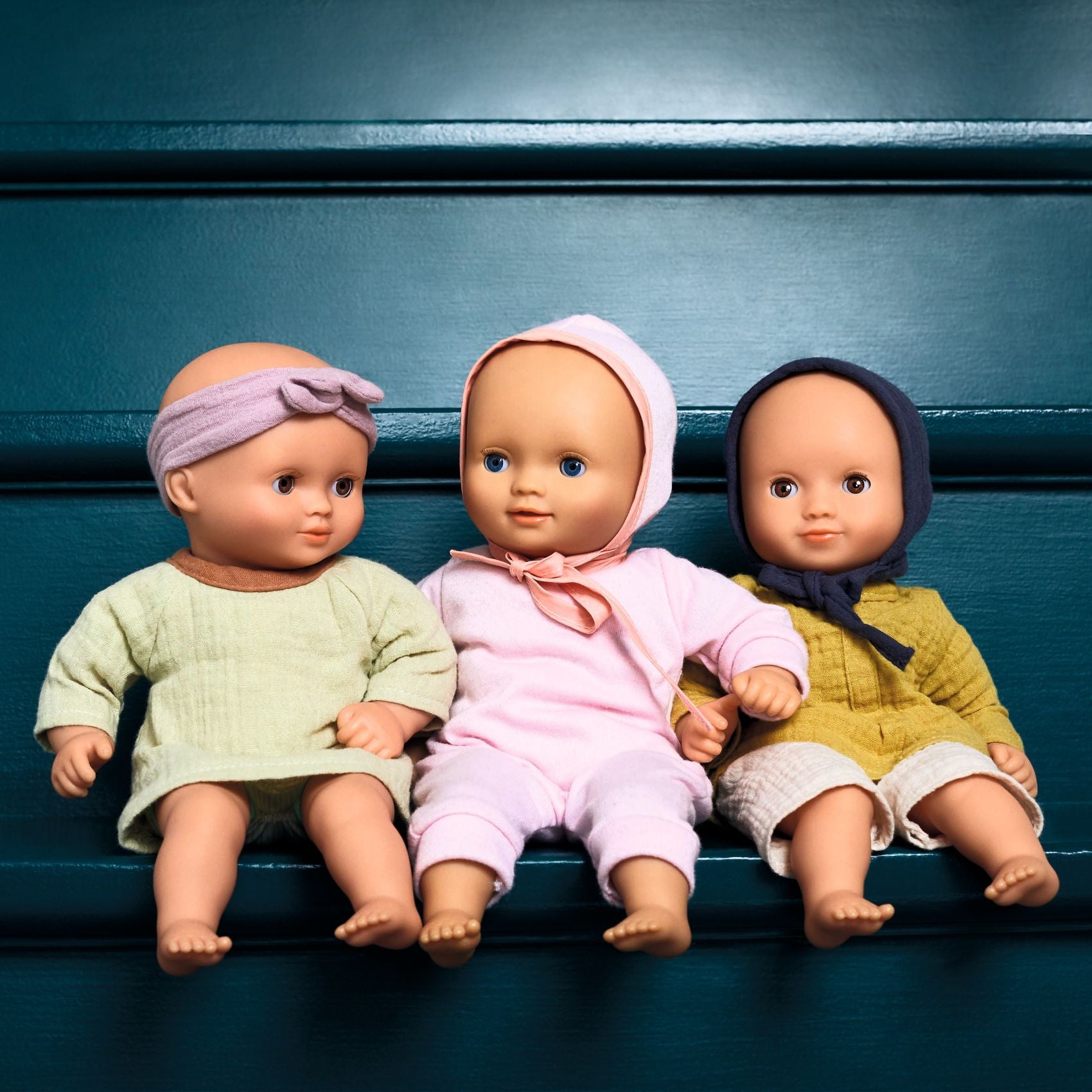 Three dolls with colorful headscarves and dresses sitting on a blue surface.