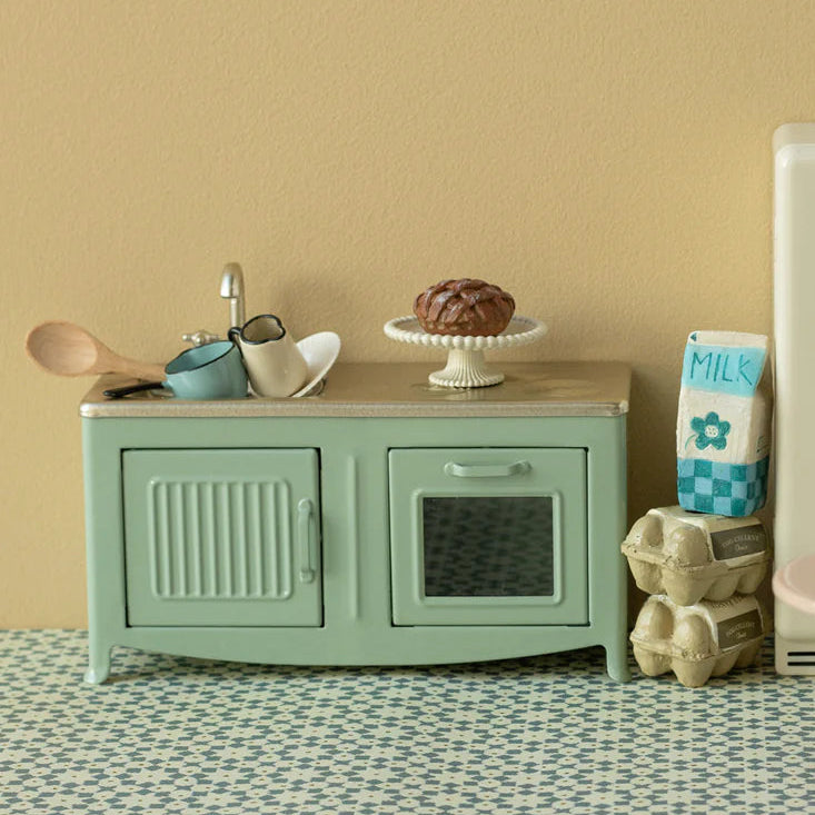Toy kitchen set with a green stove, wooden counter, and various accessories on a patterned floor.
