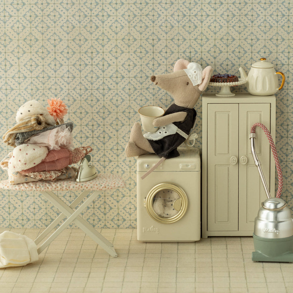 Miniature scene with a toy mouse on a washing machine, teapot, and other items against a patterned wall.