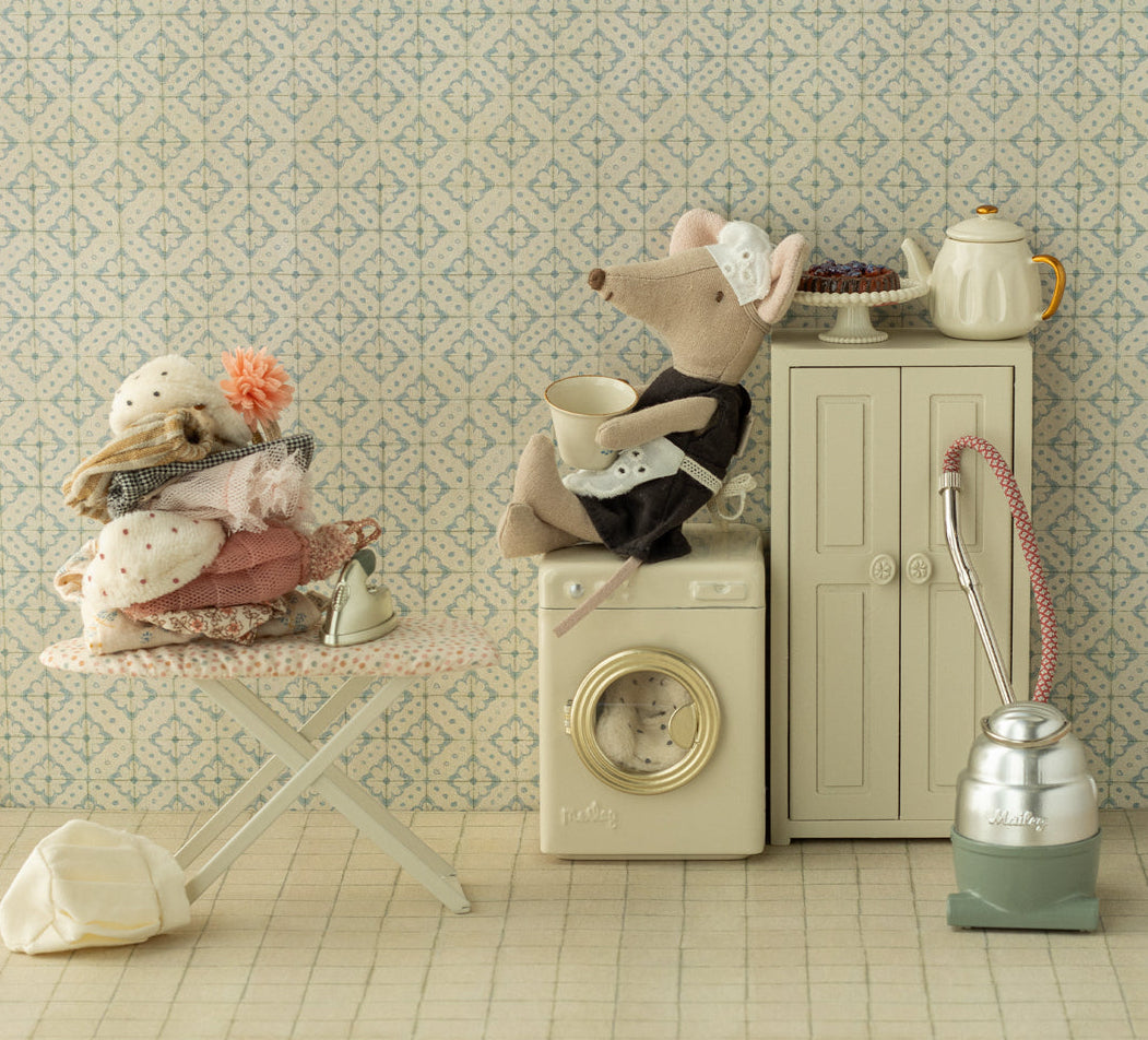Miniature scene with a toy mouse on a washing machine, teapot, and other items against a patterned wall.