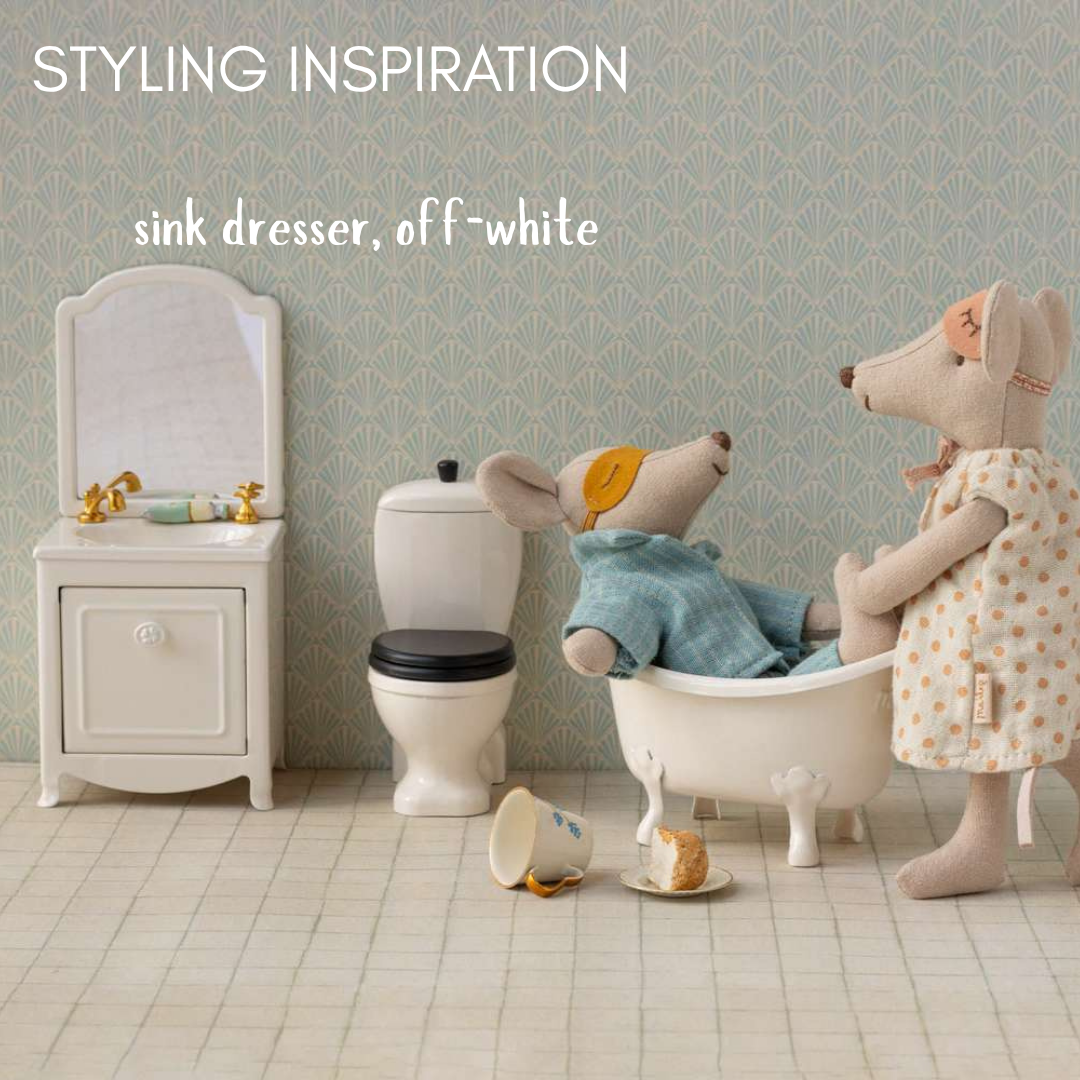 Miniature bathroom set with sink, toilet, and bathtub, featuring dolls in a stylized room.