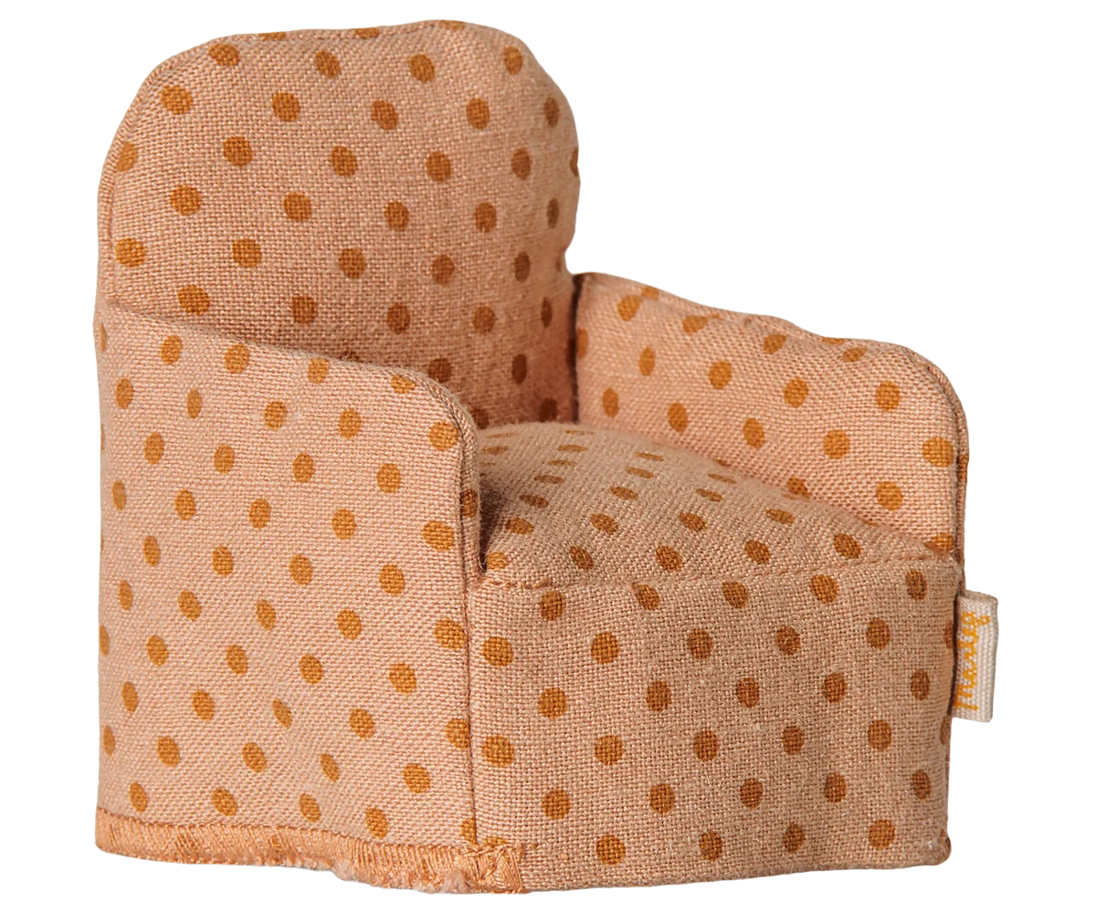 A small fabric armchair with a warm beige base and brown polka dots, photographed on a plain white background. A small fabric brand tag is visible on the right side.