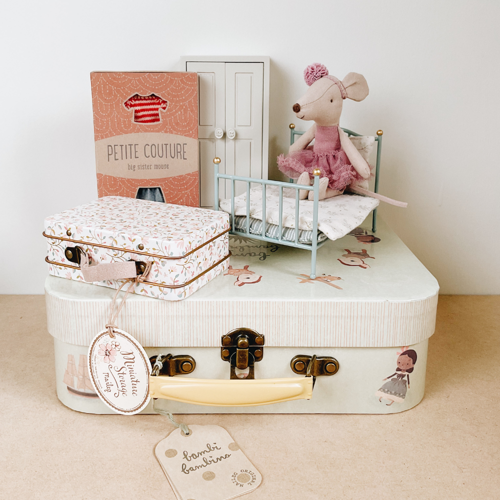 Small suitcase with a tag, toy mouse, and miniature bed on a beige surface.