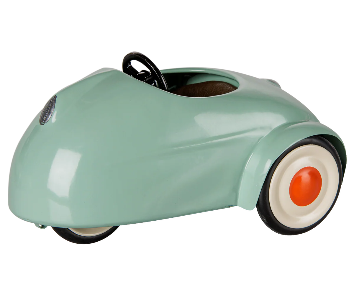 A retro-style pedal toy car in a glossy mint green finish, featuring a black steering wheel, black tires, and white-walled tires with orange center caps, shown on a plain white background.