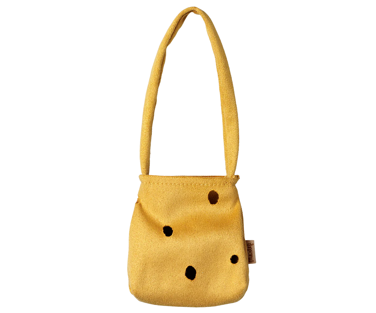 A small mustard yellow shoulder bag with a textured fabric finish, featuring black polka dots and a small brown brand tag on the side, set against a plain white background.