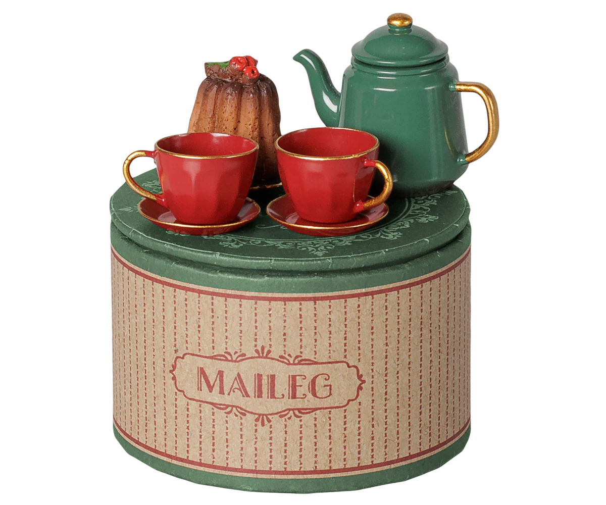 A decorative tea set displayed on a round tin canister. The set includes a green teapot with gold trim, two matching red teacups with saucers, and a small brown pumpkin decoration.