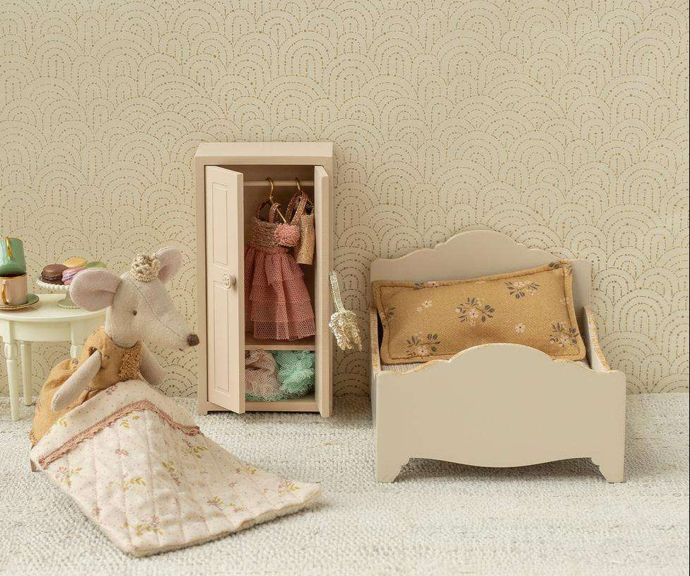 Miniature bedroom set with bed, chair, and wardrobe against a patterned wall.