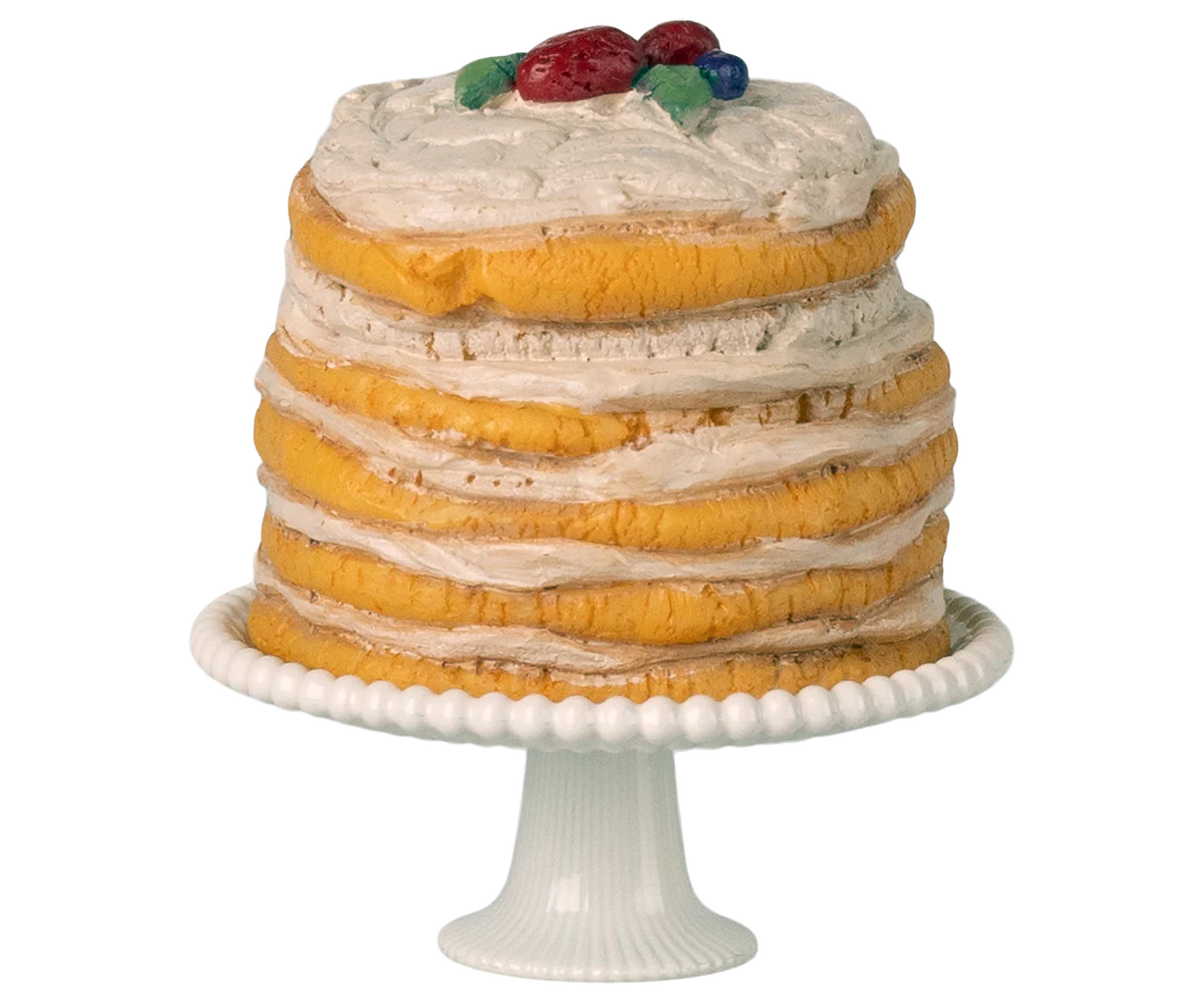 Layered cake with white frosting and fruit on top, placed on a white cake stand.