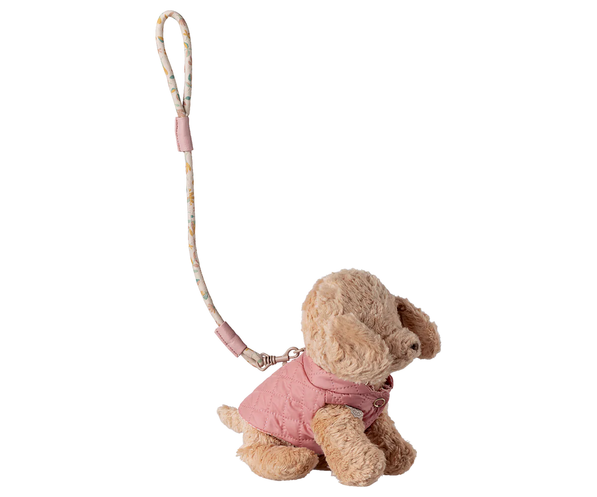 Stuffed animal toy with a pink outfit and strap on a white background