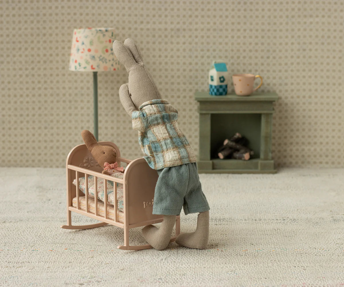 Miniature scene with a rabbit standing next to a baby crib in a cozy room.