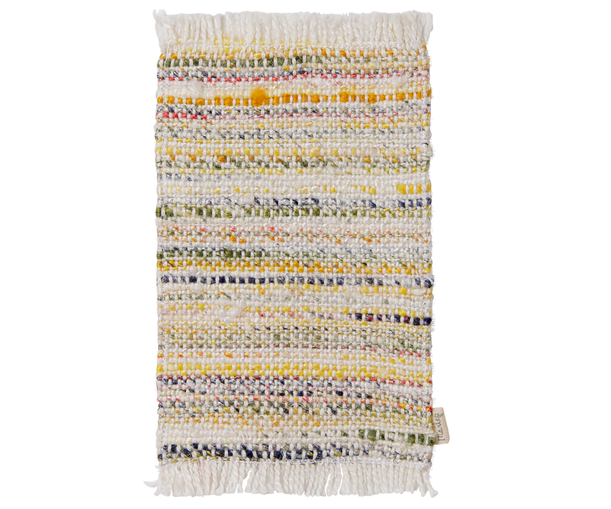 A rectangular woven rug with fringed edges, featuring horizontal stripes of yellow, green, pink, and blue threads on a cream base, shown against a plain white background.