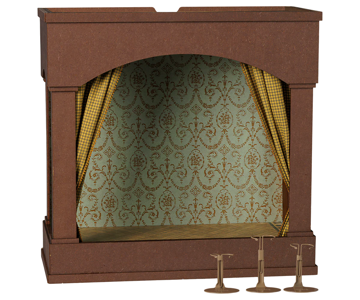 A miniature dollhouse-style fireplace or stage opening with a brown frame, patterned green and gold damask wallpaper, gold checkered curtains, and three small gold pedestal accessories on a white background.