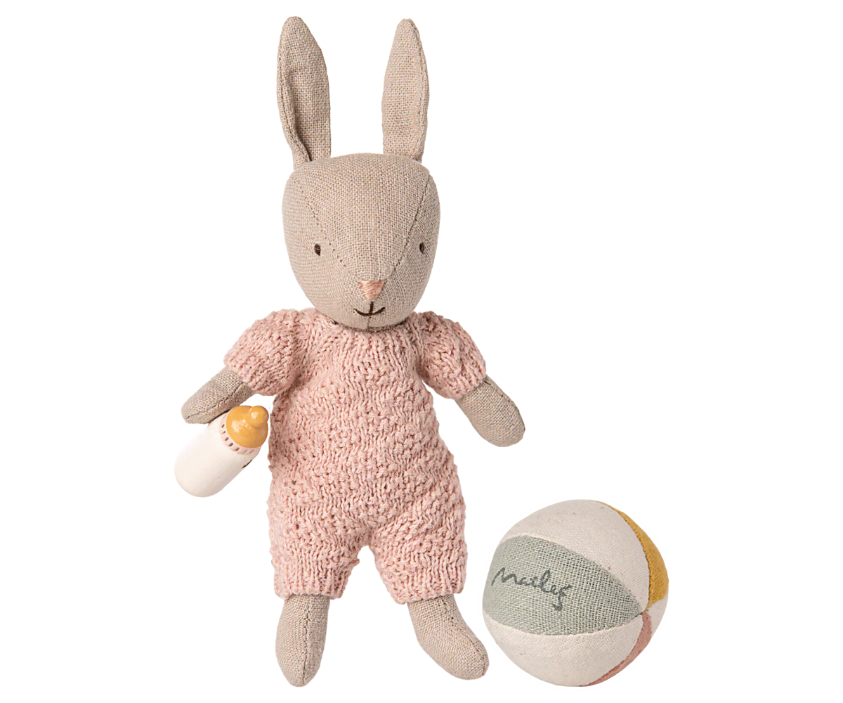 Stuffed rabbit toy in a pink outfit with a ball and bottle on a white background