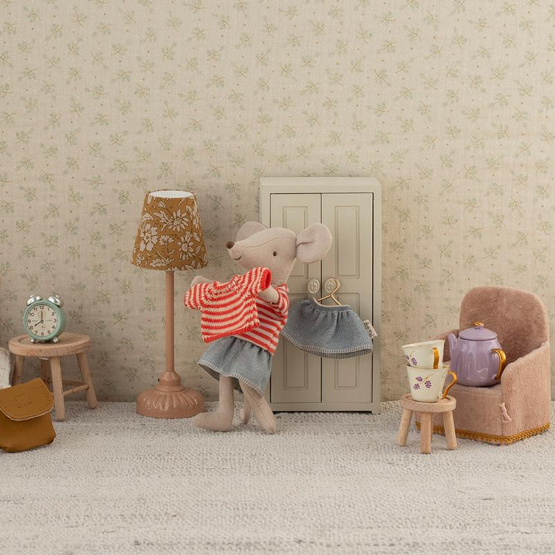 Miniature room setup with dolls and furniture against a patterned wall.