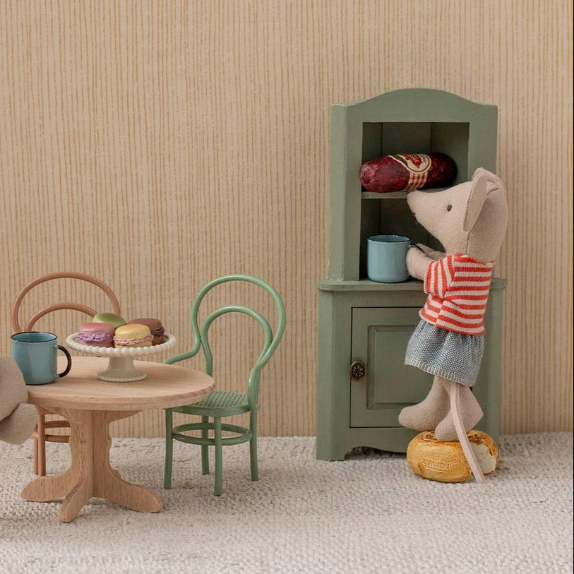 Miniature Maileg scene with toy mice around a table in a room with striped wallpaper.