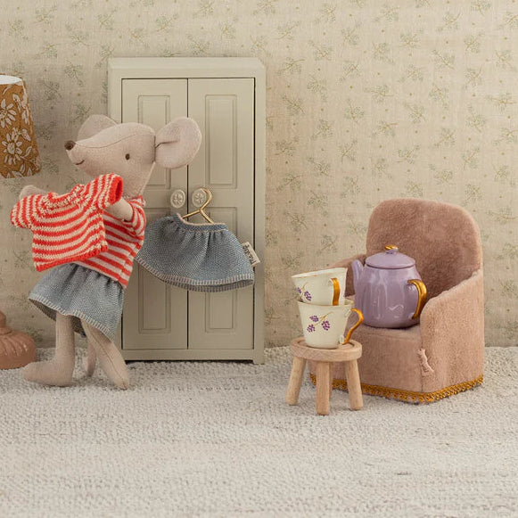 Miniature room setup with toy figures and furniture against a neutral wall.