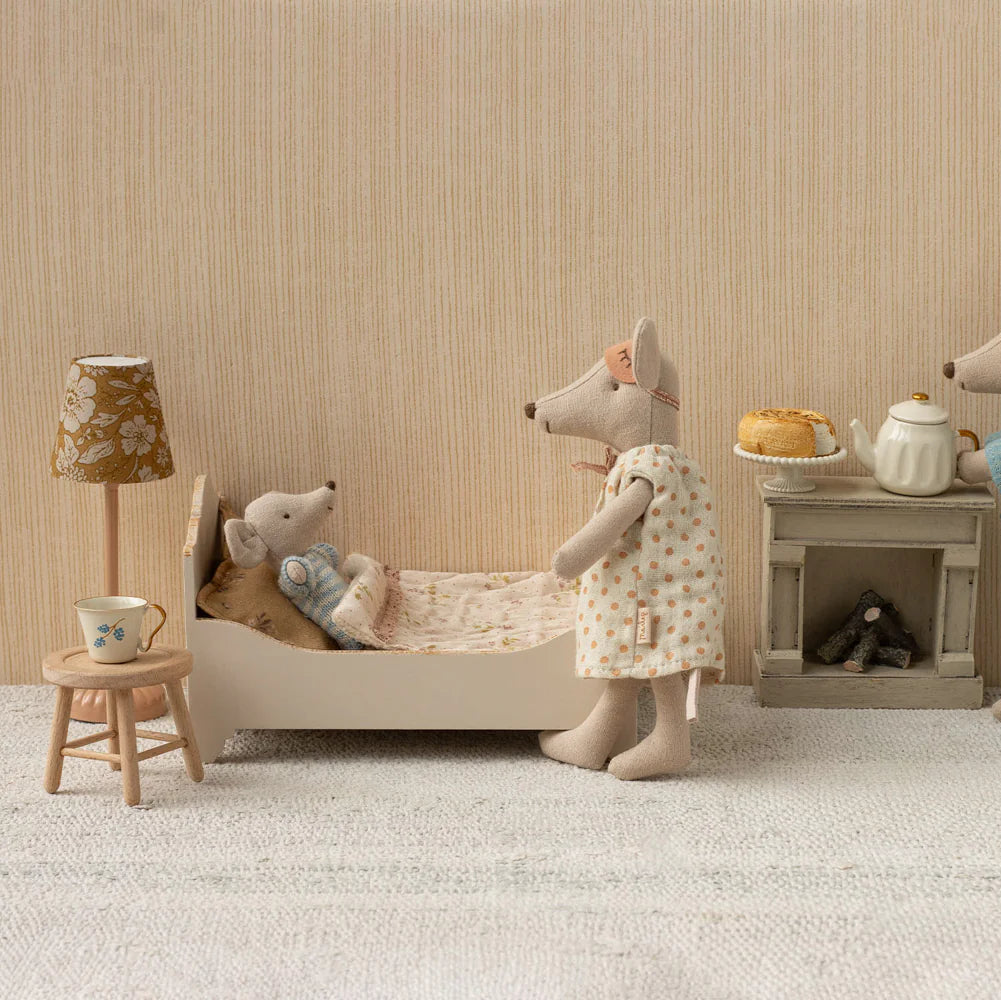 Stuffed animal toys in a room setting with a bed, lamp, and small table.
