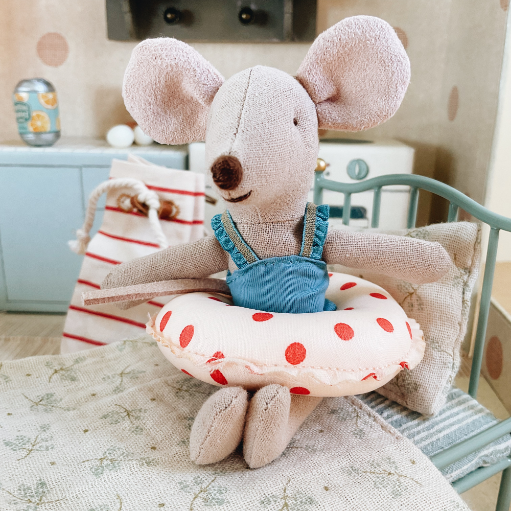 Stuffed mouse toy with a life preserver on a miniature chair in a cozy room setting.