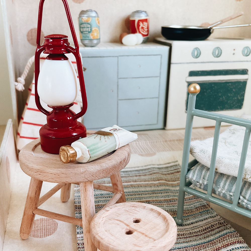 Miniature kitchen scene with red lantern, wooden stool, and vintage-style oven.