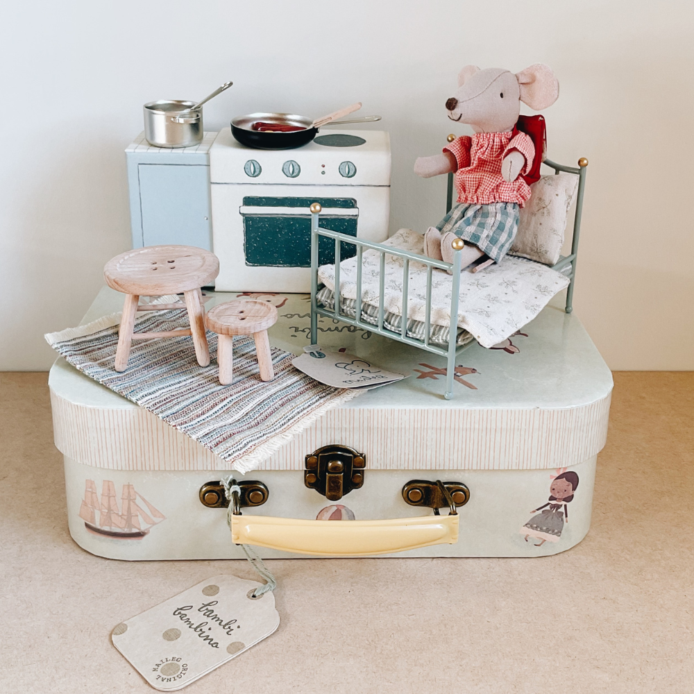 Toy kitchen set with a suitcase, stove, oven, and mouse figure on a beige surface.
