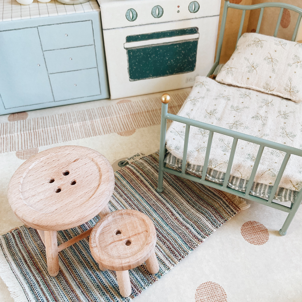 Maileg mouse kitchen with toy stove, cabinets, and bed on a patterned rug.