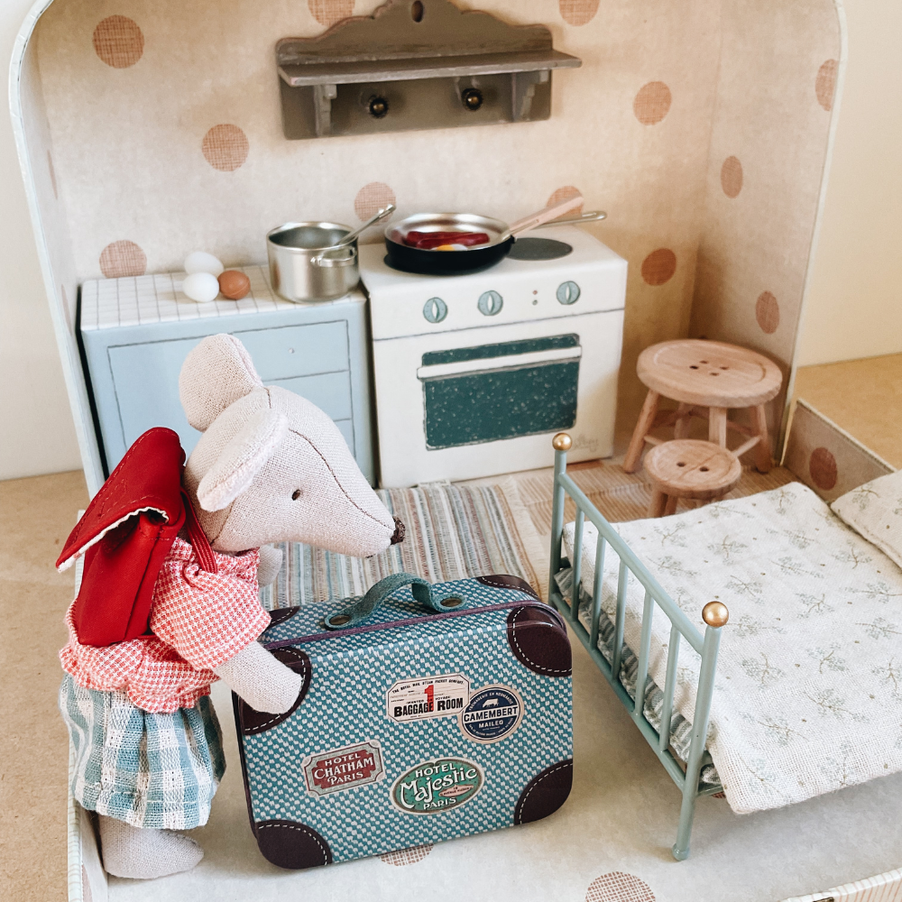 Miniature dollhouse kitchen with stove, oven, and refrigerator, featuring a mouse character with a suitcase.