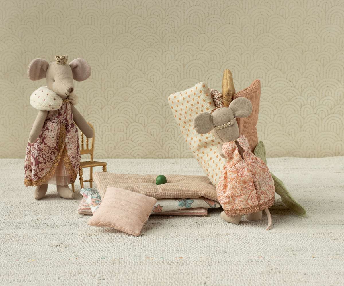 Two plush mouse toys with floral dresses on a textured surface with a patterned wall in the background.