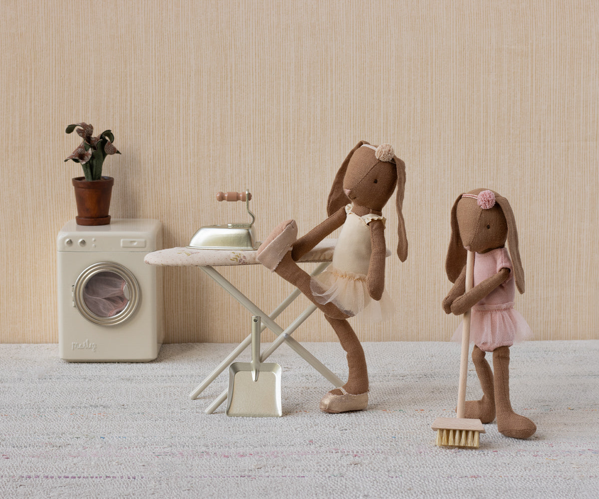 Two Maileg toy bunnies in a domestic setting with a washing machine and ironing board.