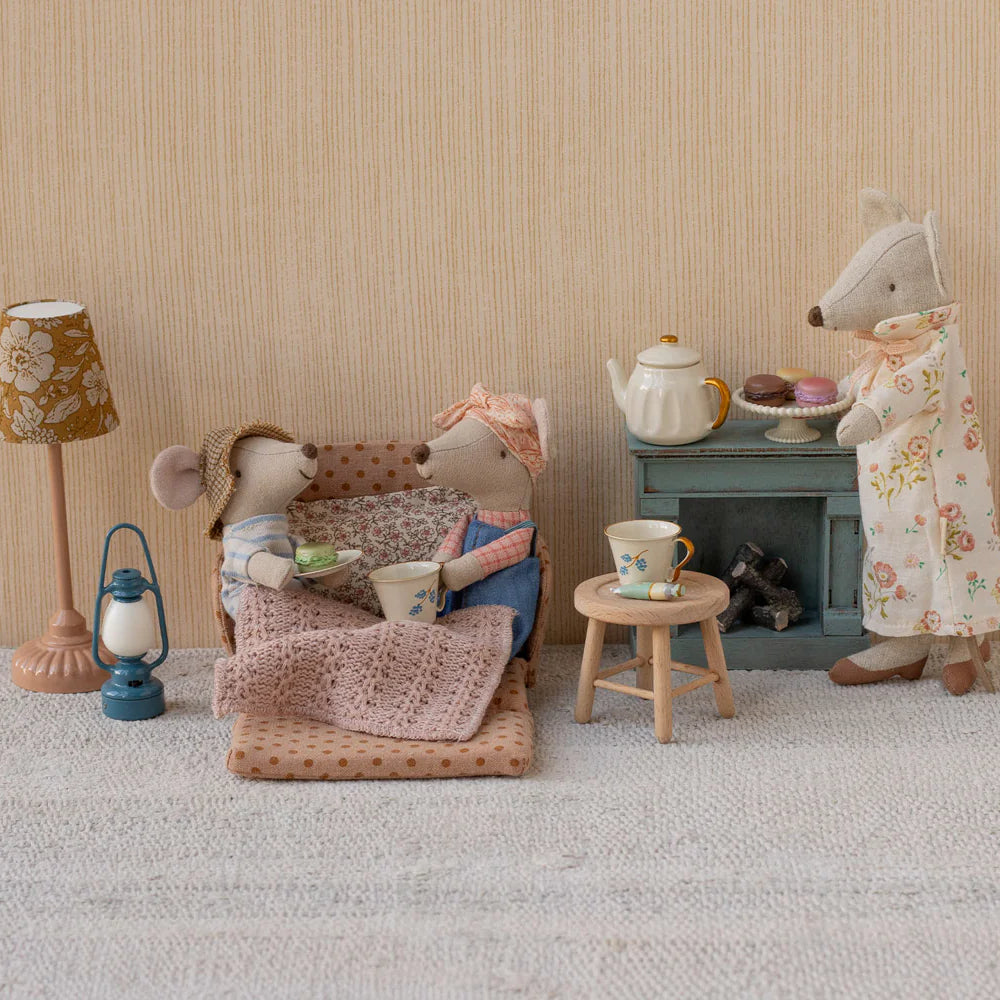 Miniature scene with toy mice and tea set against a beige wall.