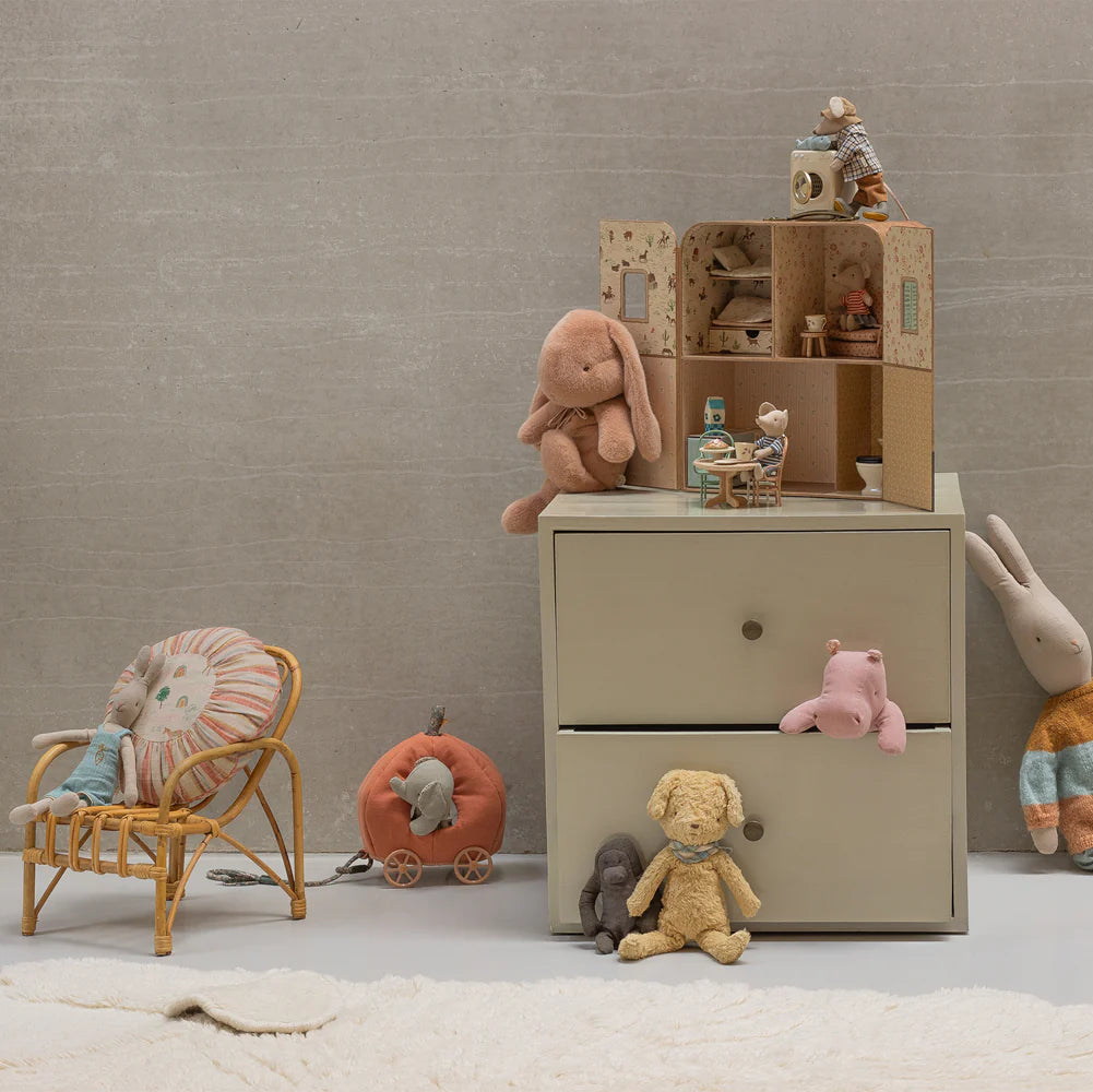 Children's room with a dresser, toys, and a chair against a plain wall and Maileg suitcasa dolls house