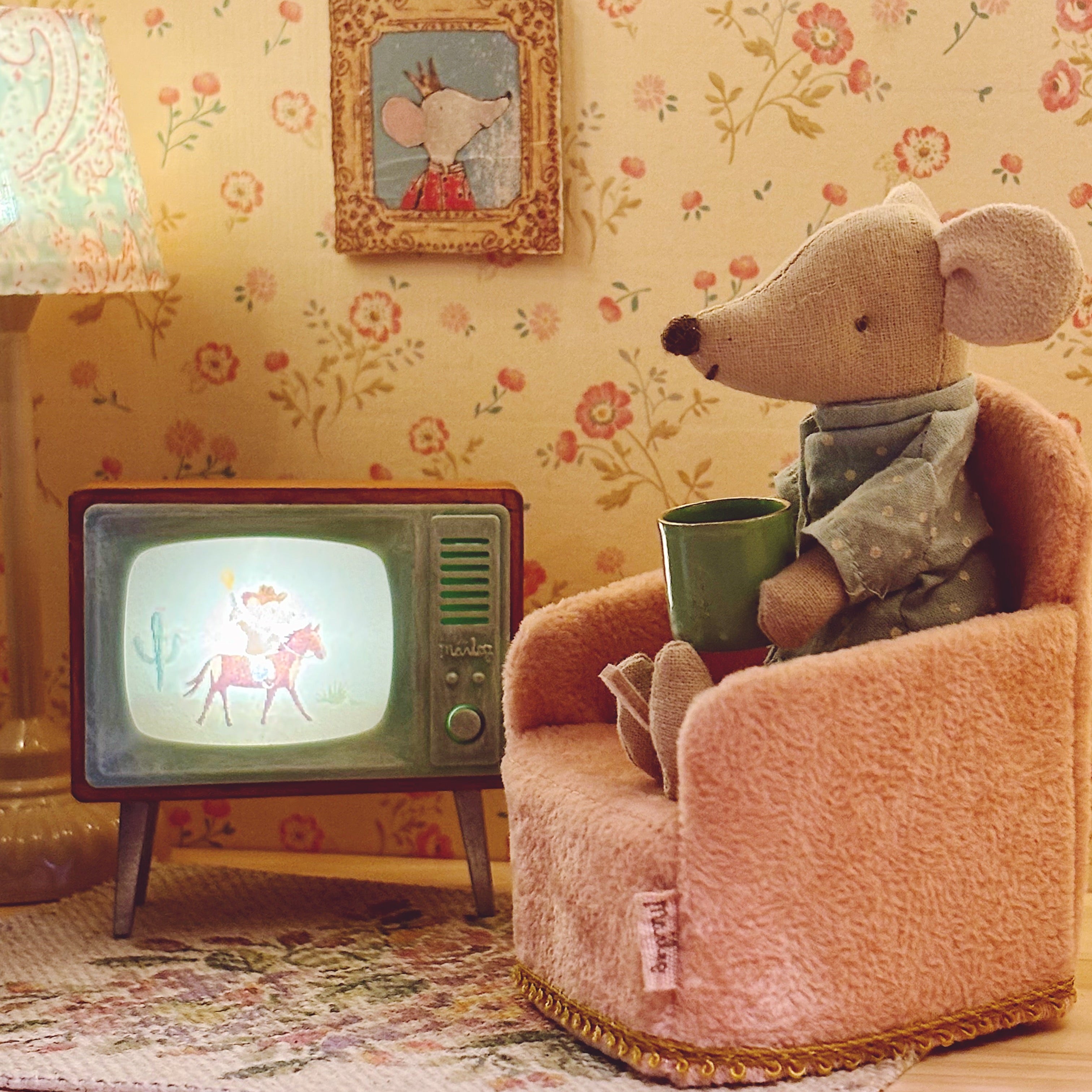 MAileg mouse wearing pyjamas sitting an armchair watching the television in a dolls house living room scene