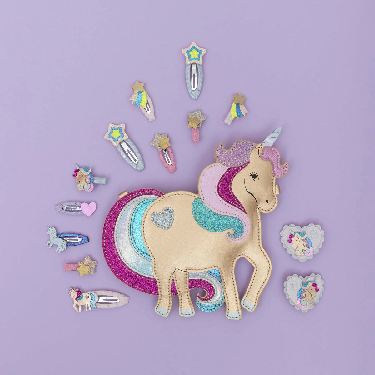 A unicorn-themed craft or costume accessory set arranged on a lavender background. The set includes a beige faux-leather unicorn body with a pink and purple horn, a multicolored tail, several hair clips, and heart-shaped pins featuring unicorn illustrations.