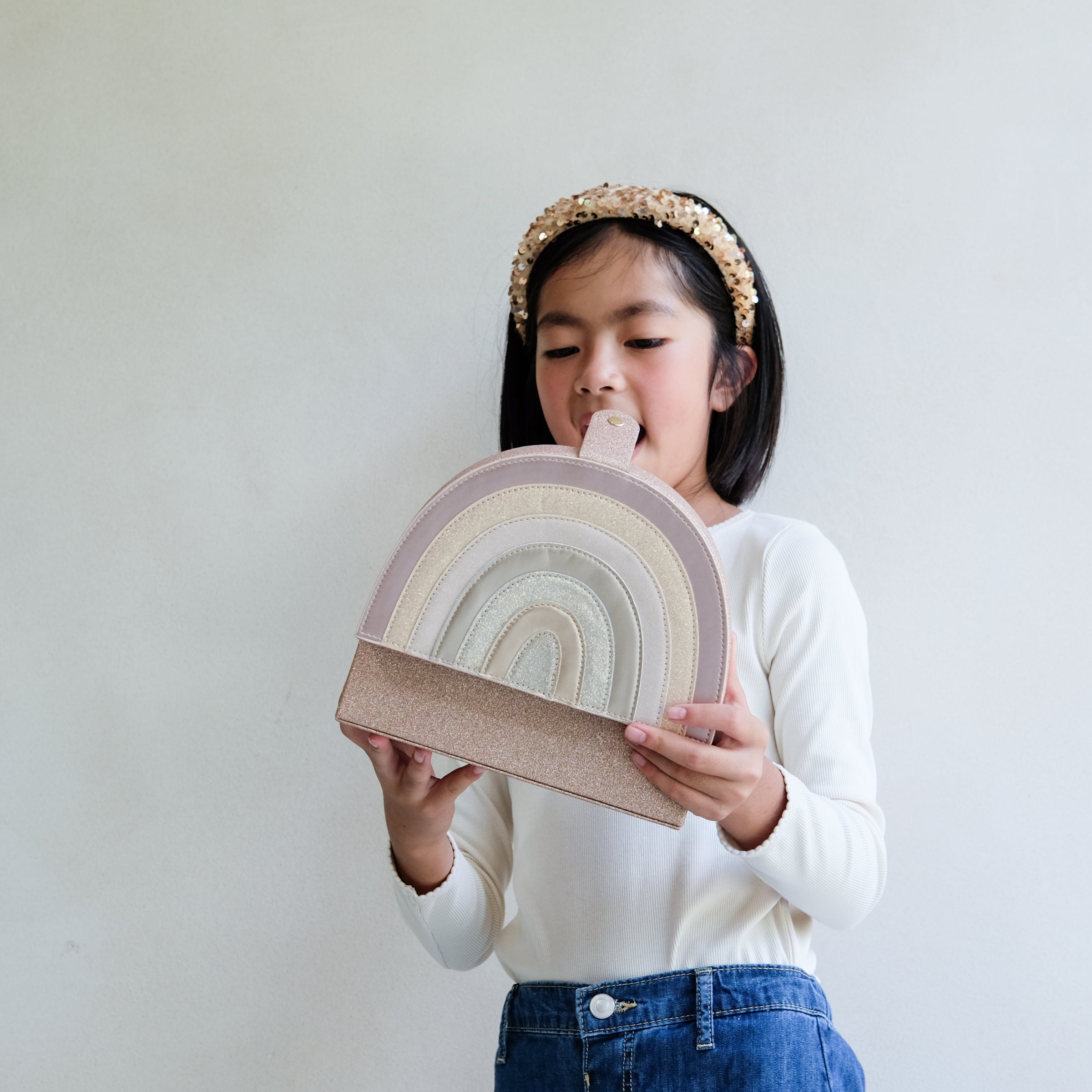 Child holding a rainbow-shaped jewelllery box against a plain background