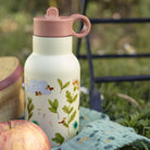 Floral-patterned water bottle with pink lid on a picnic blanket outdoors