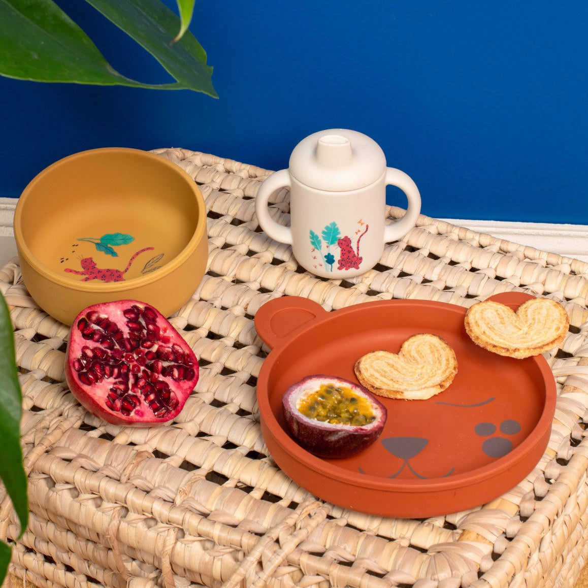 Children's tableware set with a bowl, mug, and plate on a woven surface against a blue background.
