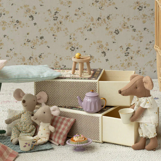 Miniature Maileg mouse toy setup with mice around a table and chair, against a floral wallpaper background.