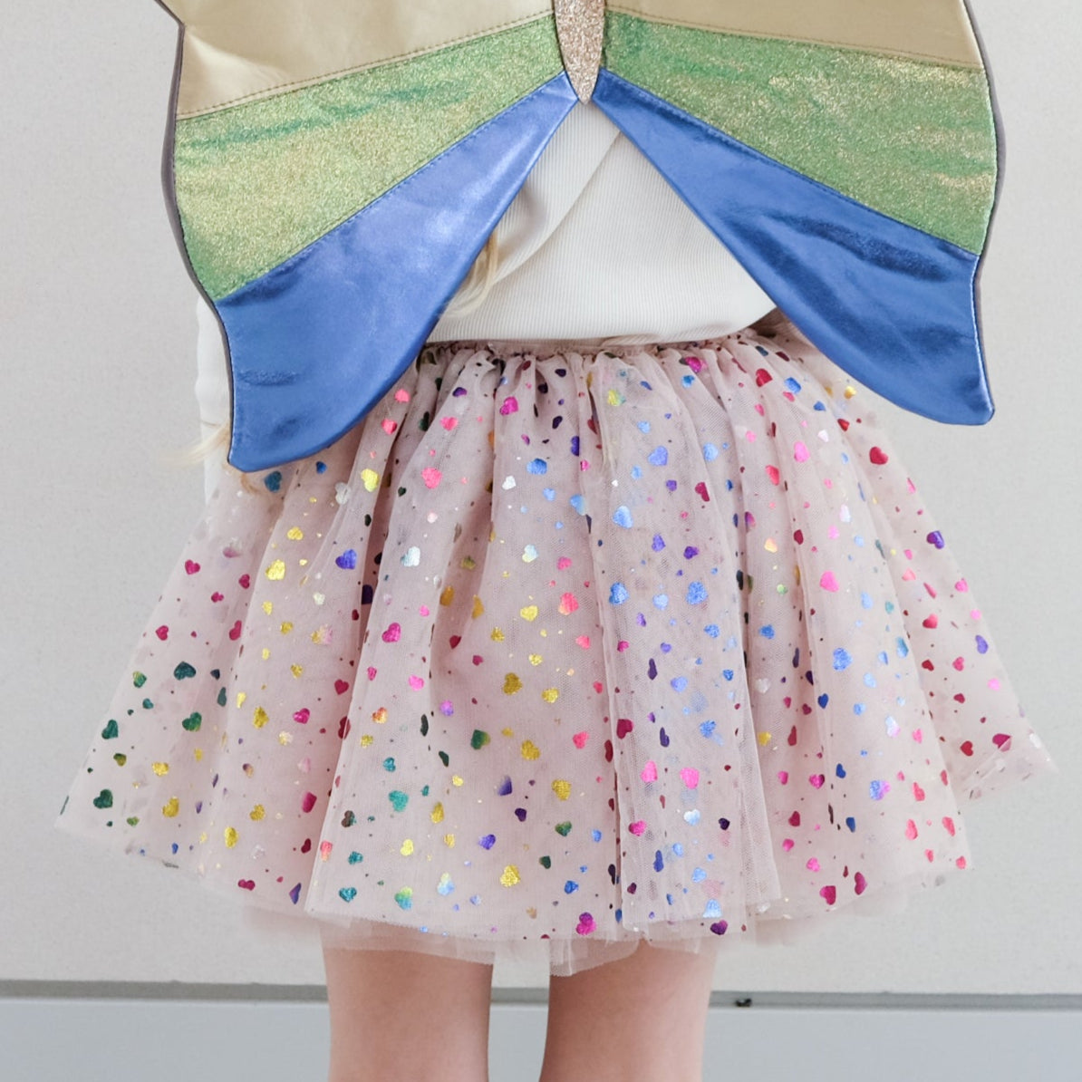 Child wearing colorful tutu with heart embellishments against a plain background