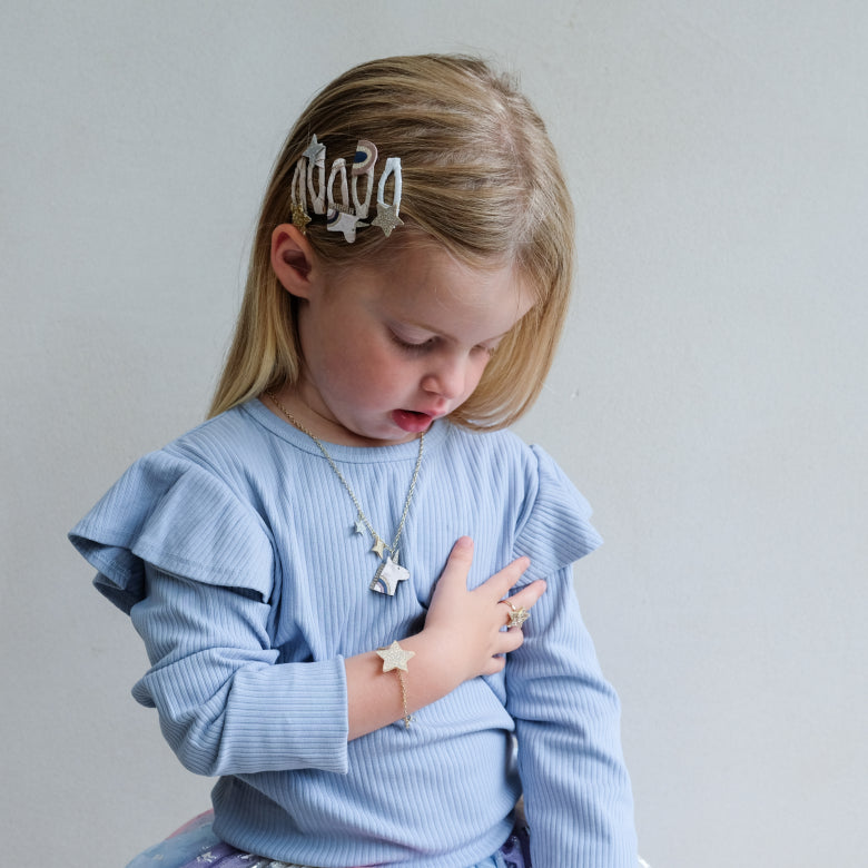 Young girl wearing a blue sweater and unicorn jewellery with a neutral background